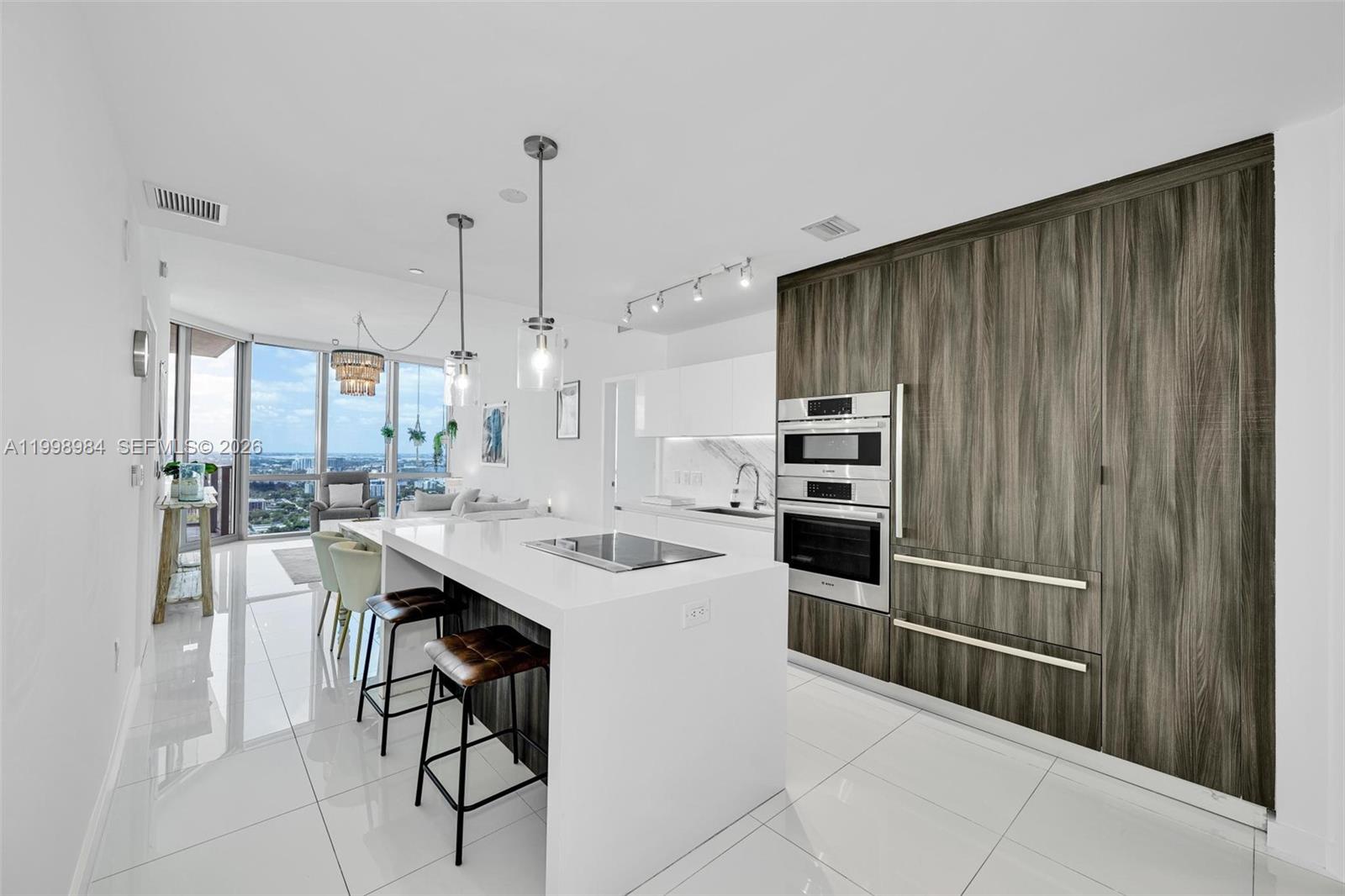 A modern kitchen features a white island with a cooktop, wood-paneled cabinetry, and floor-to-ceiling windows — 851 NE 1st Ave # 3708, Miami FL 33132, MIAMI, FL