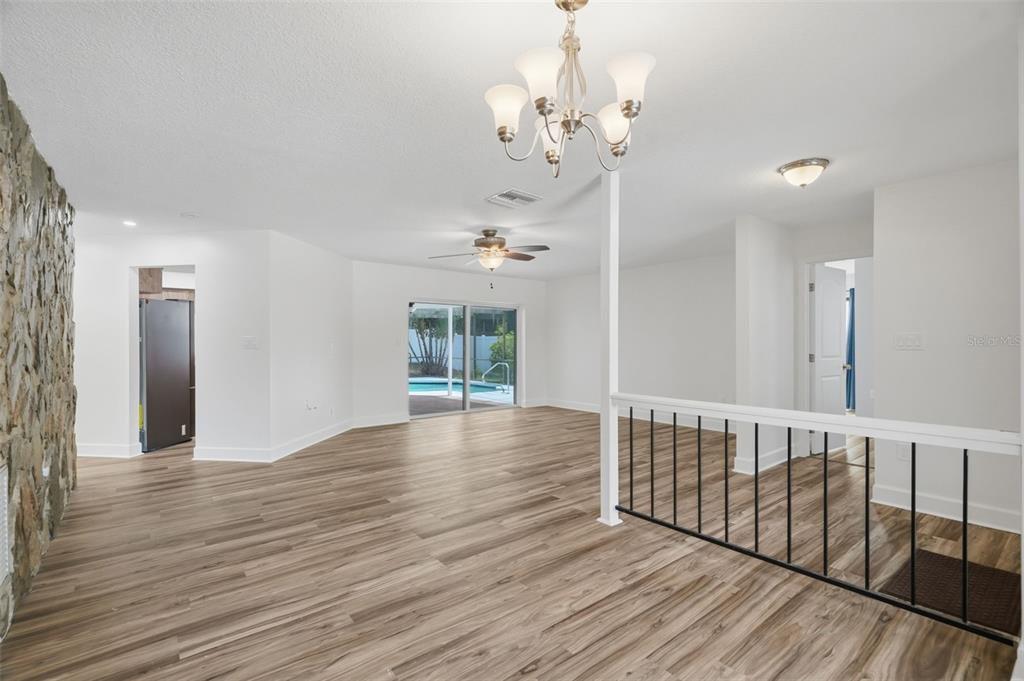 An open-concept living area features wood-look flooring, a stone accent wall, and a pool view — 104 NESTLEBRANCH DRIVE, SAFETY HARBOR, FL