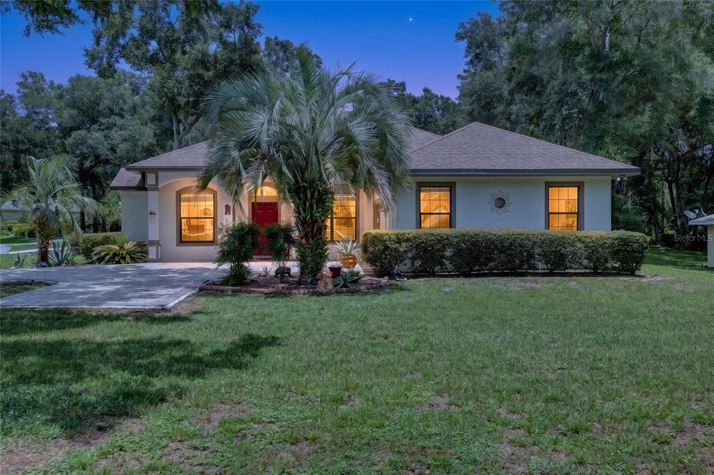 A single-story house with a red front door, palm tree, and lawn at dusk — 19331 SW 100TH LOOP, DUNNELLON, FL