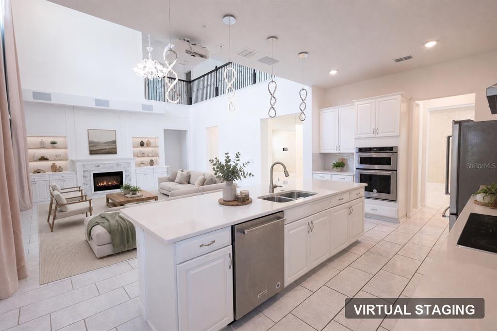 A bright, open-concept kitchen and living area featuring white cabinetry, a large island, and fireplace — 9567 MEADOW HUNT WAY, WINTER GARDEN, FL