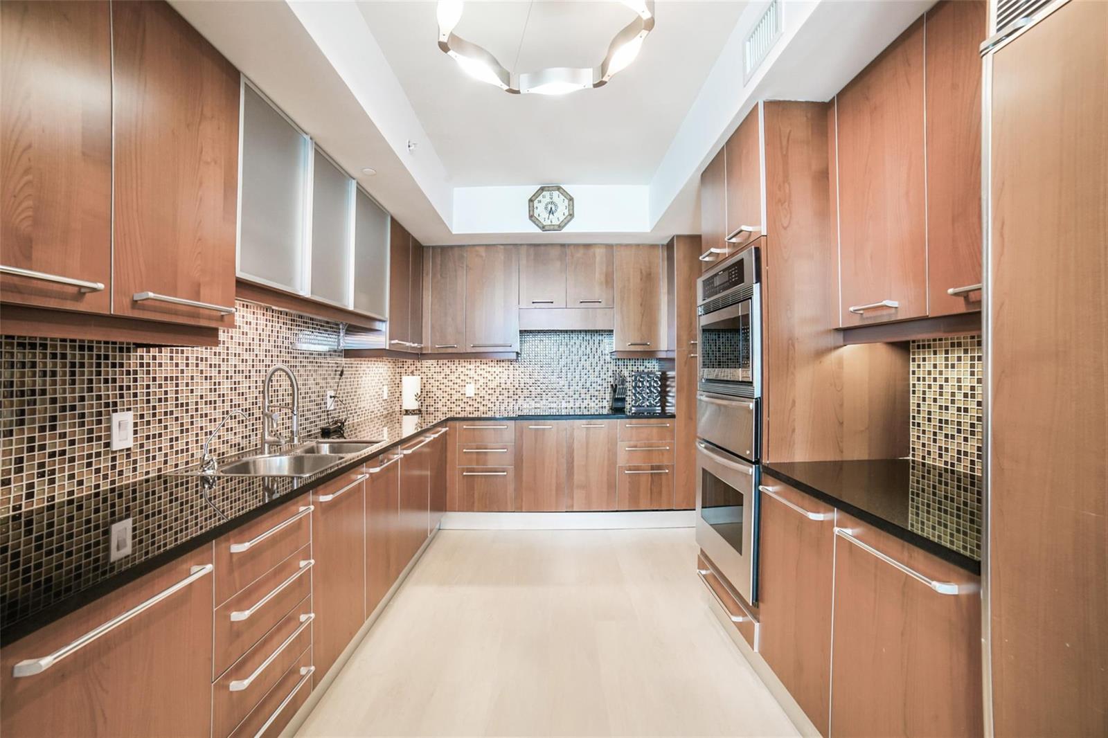 A galley kitchen features wood cabinets, black countertops, a mosaic tile backsplash, and stainless appliances — 3101 S Ocean Drive # 401, Hollywood FL 33019, HOLLYWOOD, FL