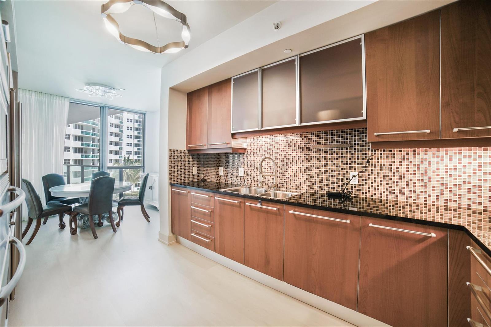 A modern kitchen features wood cabinets, black countertops, and a mosaic tile backsplash — 3101 S Ocean Drive # 401, Hollywood FL 33019, HOLLYWOOD, FL