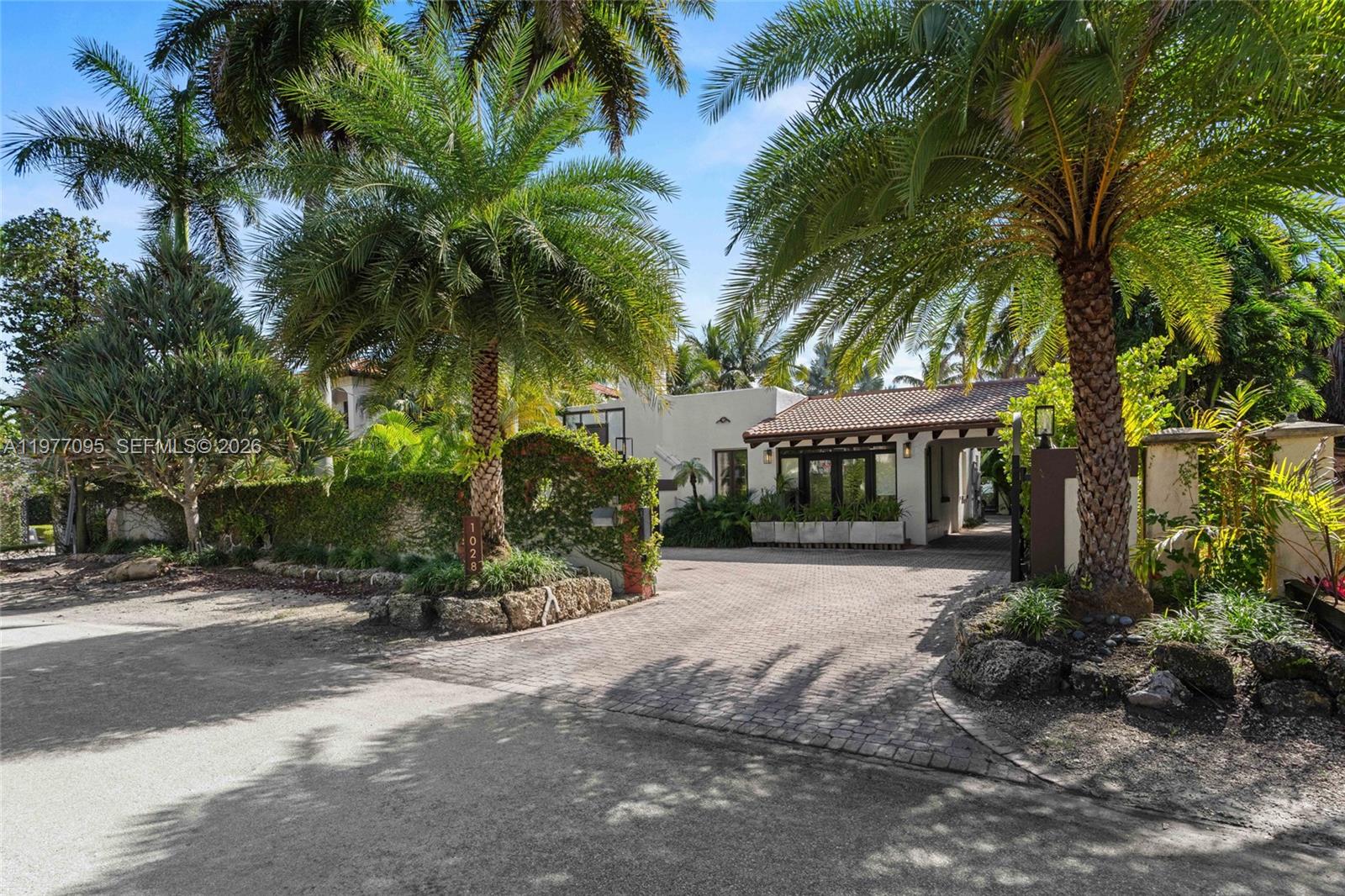 A paved driveway leads to a white house entrance framed by palm trees and landscaping — 1028 NE 84th St, Miami FL 33138, MIAMI, FL