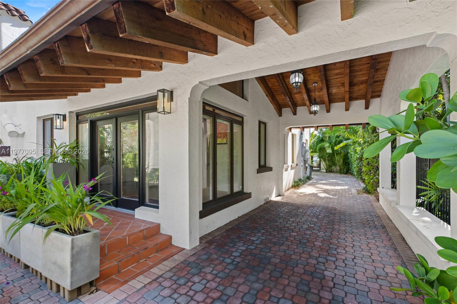 A covered brick driveway leads to a home entrance with a wooden beamed ceiling — 1028 NE 84th St, Miami FL 33138, MIAMI, FL