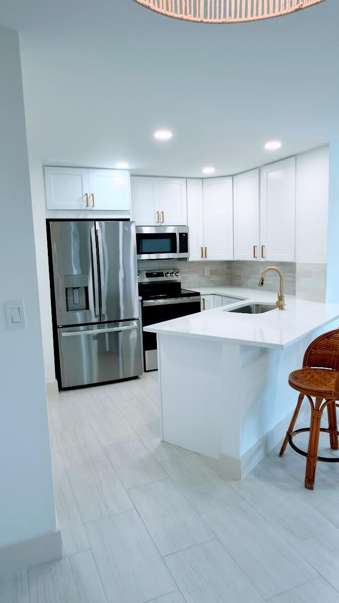 A modern kitchen features white cabinets, stainless steel appliances, a quartz countertop, and a peninsula — 7547 S Oriole Boulevard # 101, Delray Beach FL 33446, DELRAY BEACH, FL
