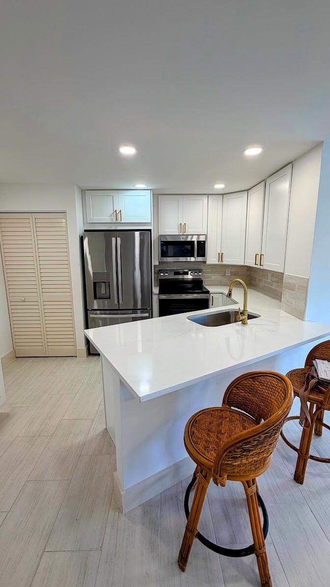 A kitchen featuring white cabinets, stainless steel appliances, a quartz island, and wicker bar stools — 7547 S Oriole Boulevard # 101, Delray Beach FL 33446, DELRAY BEACH, FL