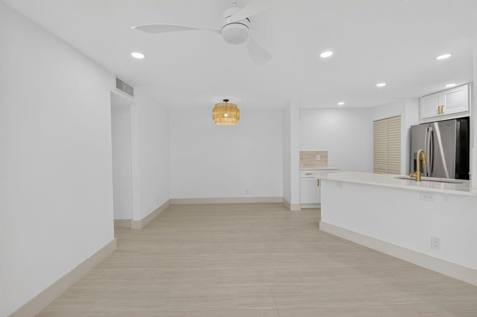A bright, open-concept dining area features light wood-look tile flooring and a modern drum chandelier — 7547 S Oriole Boulevard # 101, Delray Beach FL 33446, DELRAY BEACH, FL