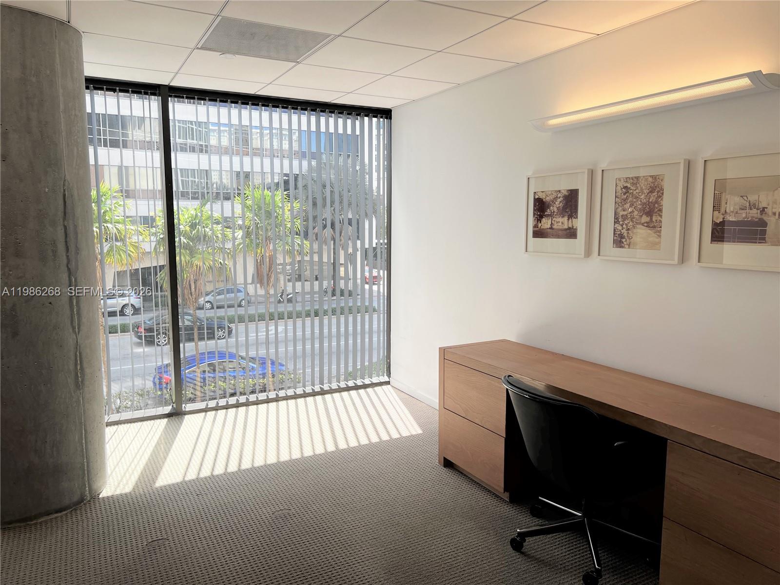 A modern office features a wooden desk, a black chair, and large windows with blinds — 2100 Ponce De Leon Blvd, Coral Gables FL 33134, CORAL GABLES, FL