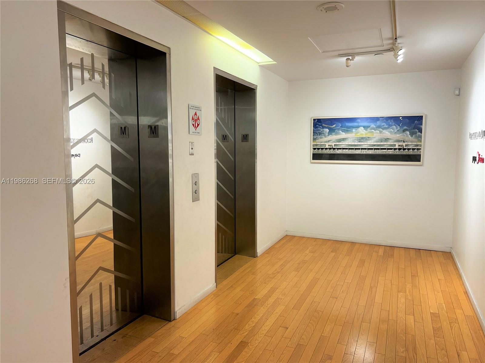 An elevator lobby features two stainless steel doors, hardwood flooring, and a framed wall painting — 2100 Ponce De Leon Blvd, Coral Gables FL 33134, CORAL GABLES, FL