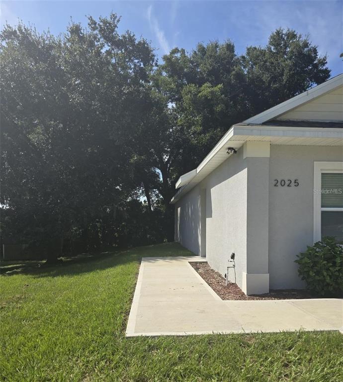 A concrete walkway leads along the side of a gray house toward large trees — 2025 DUNBAR ST, BARTOW, FL