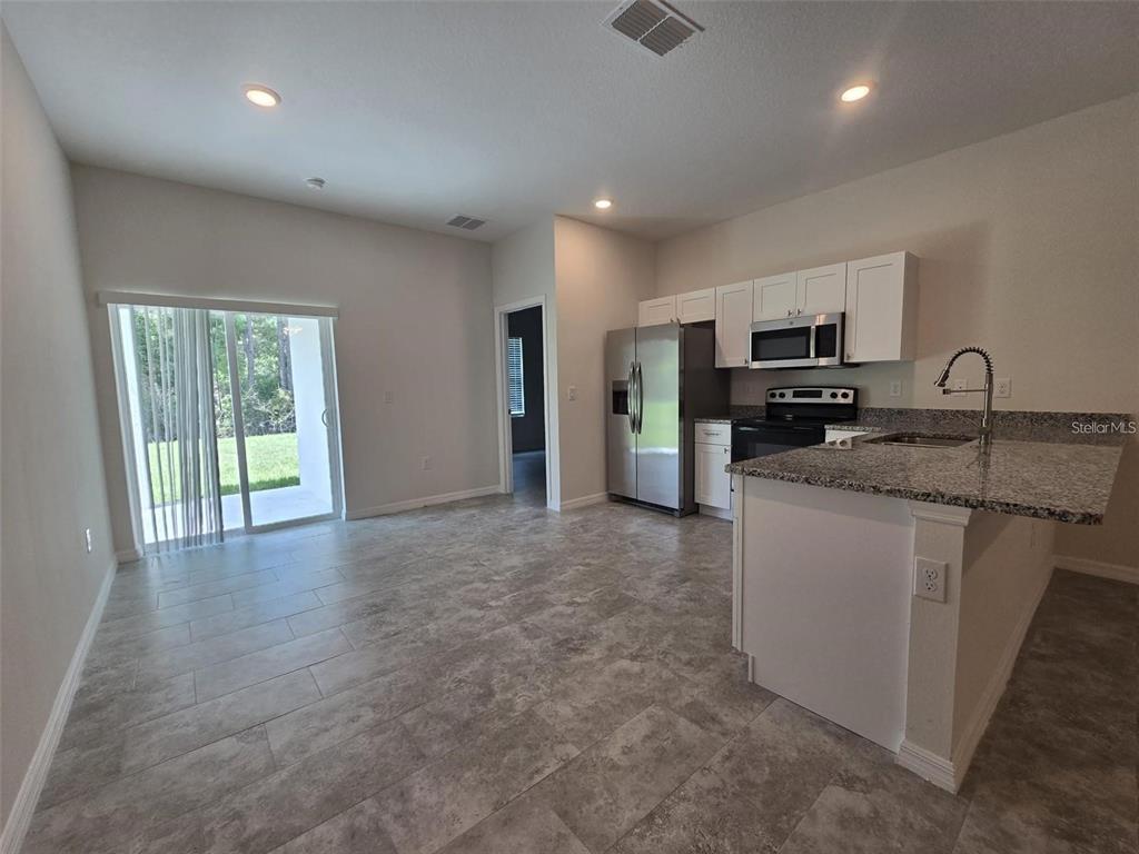 A kitchen with white cabinets, stainless steel appliances, and granite countertops opens to a living area — 2025 DUNBAR ST, BARTOW, FL
