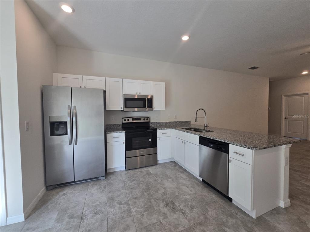 A kitchen features white cabinets, stainless steel appliances, granite countertops, and gray tile flooring — 2025 DUNBAR ST, BARTOW, FL