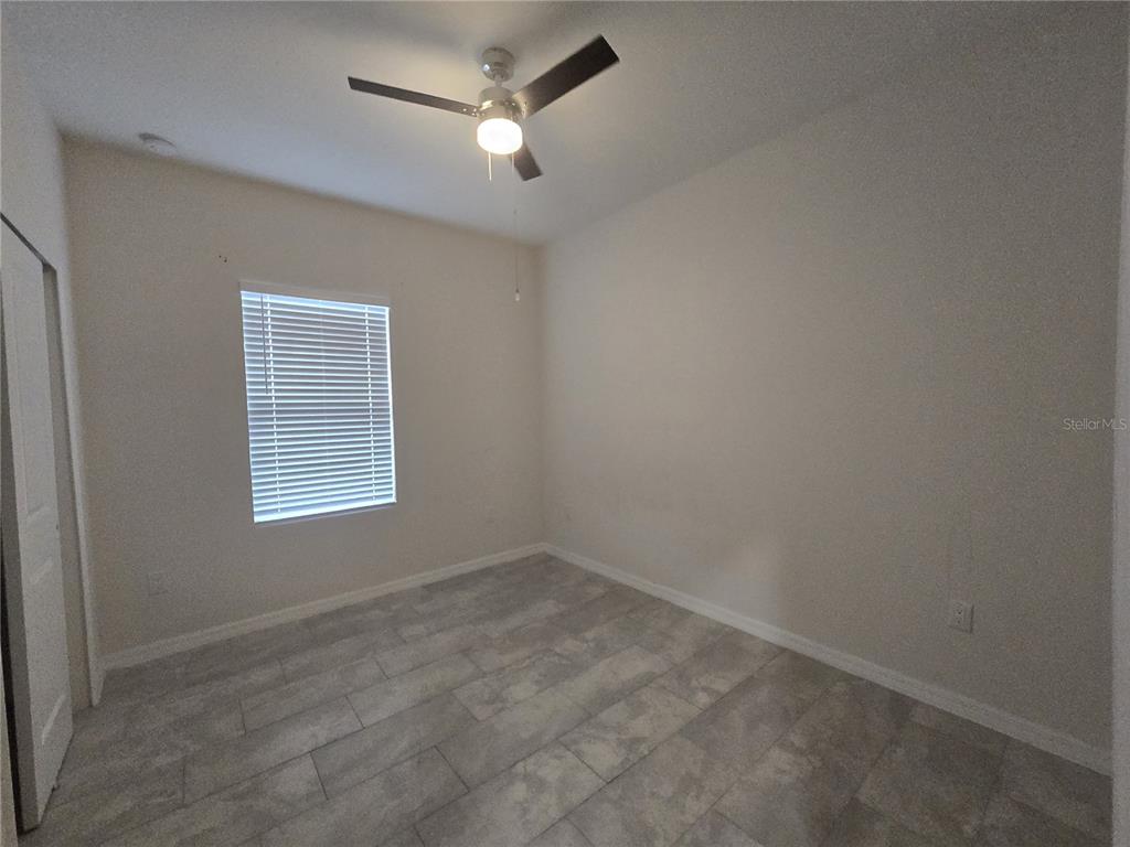 An empty bedroom features light-colored walls, a ceiling fan, a window with blinds, and tiled flooring — 2025 DUNBAR ST, BARTOW, FL