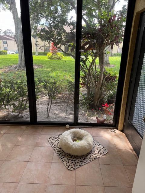 A tiled sunroom features a fluffy pet bed on a patterned mat by sliding doors — 440 Pine Glen Lane # 1, FL 33463, FL