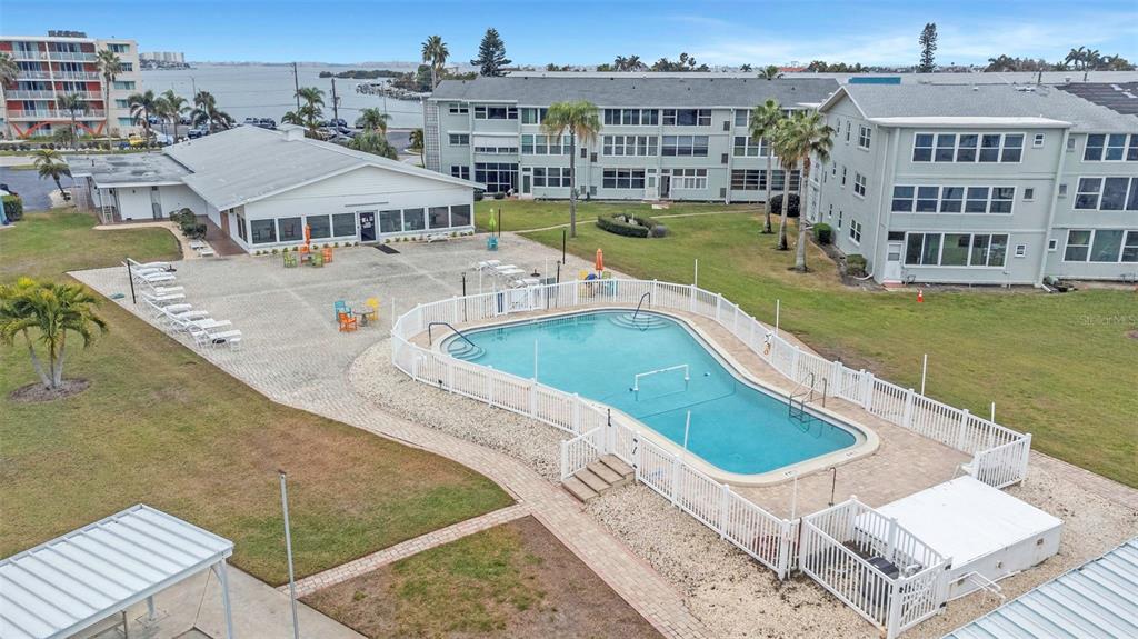An aerial view shows a swimming pool, a clubhouse, and apartment buildings near the water — 1893 SHORE DRIVE S UNIT 114, SOUTH PASADENA, FL