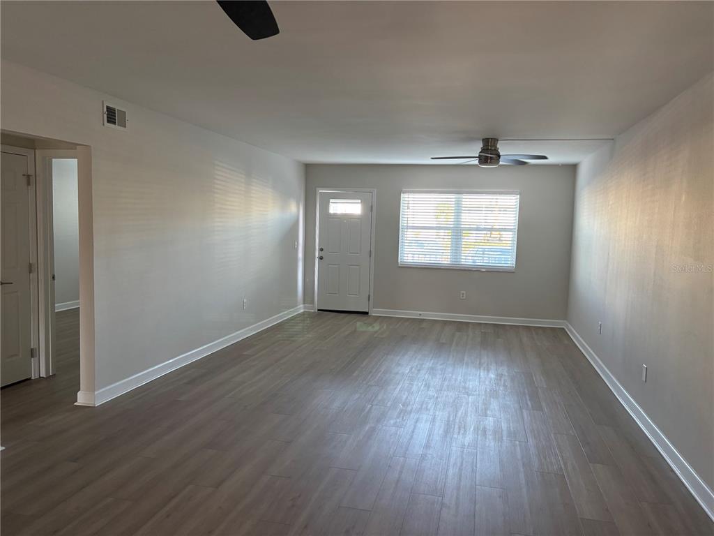 An empty living room features light gray walls, wood-look flooring, a ceiling fan, and windows — 1893 SHORE DRIVE S UNIT 114, SOUTH PASADENA, FL