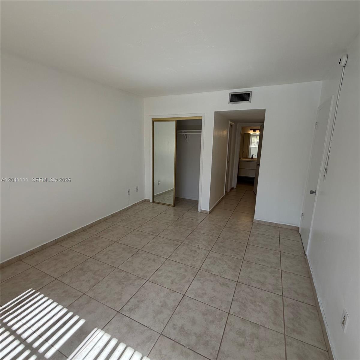 An empty bedroom with white walls, tiled floors, a mirrored closet, and an adjacent bathroom — 7505 SW 82nd St # 206, Miami FL 33143, MIAMI, FL