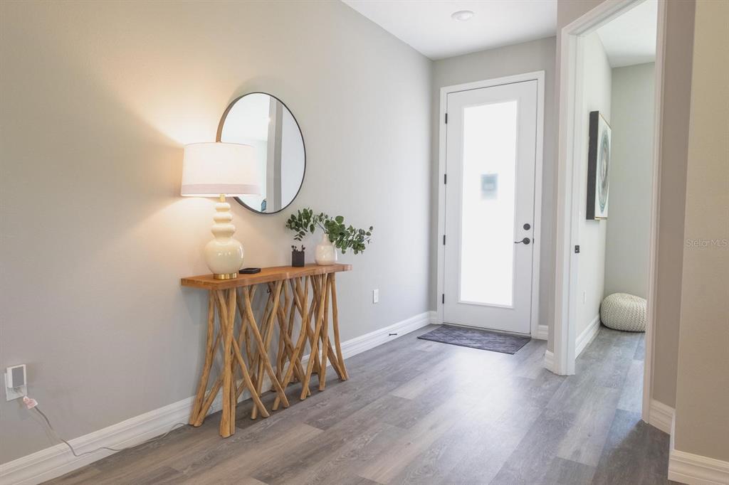 A bright entryway features a wooden console table, a round mirror, and gray flooring — 13400 SW 77TH COURT, OCALA, FL