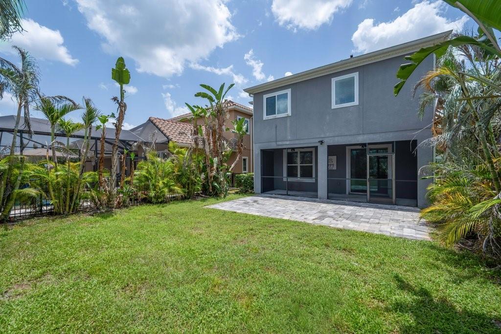 The backyard features a paved patio, a grassy lawn, and a two-story gray house — 14306 BARRINGTON STOWERS DRIVE, LITHIA, FL
