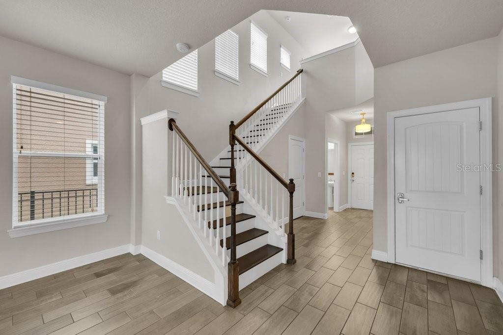 A foyer features wood-look tile flooring, a white staircase with a wooden handrail, and windows — 14306 BARRINGTON STOWERS DRIVE, LITHIA, FL