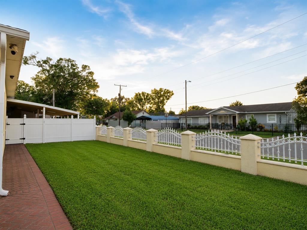 A grassy backyard features a brick walkway, a white privacy fence, and decorative metal fencing — 6922 N HALE AVENUE, TAMPA, FL