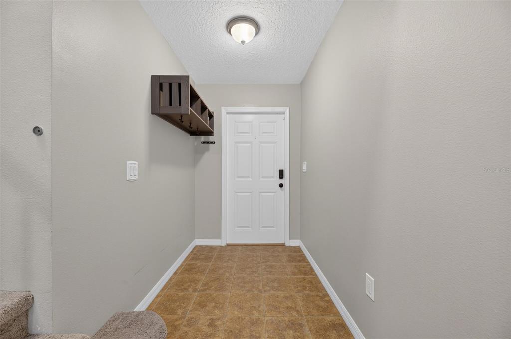 An entryway features tan tile flooring, a white door, and a dark wood wall-mounted shelf — 7842 CARRIAGE POINTE DRIVE, GIBSONTON, FL
