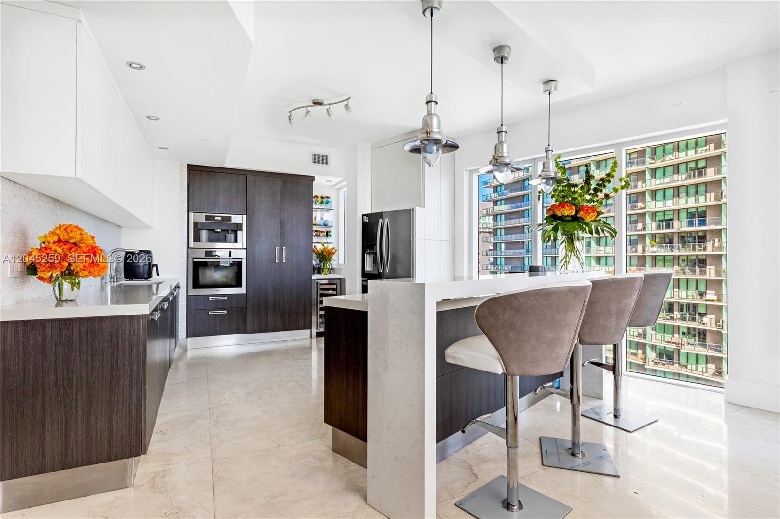 A modern kitchen features dark wood cabinetry, white countertops, a breakfast bar, and city views — 60 SW 13th St # 3200, Miami FL 33130, MIAMI, FL