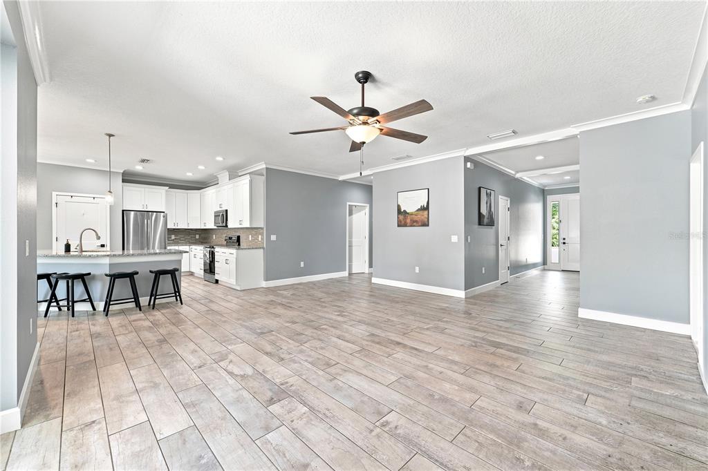 An open-concept kitchen and living area feature light wood-look tile flooring and white cabinetry — 125 LONGWOOD DRIVE, OSTEEN, FL