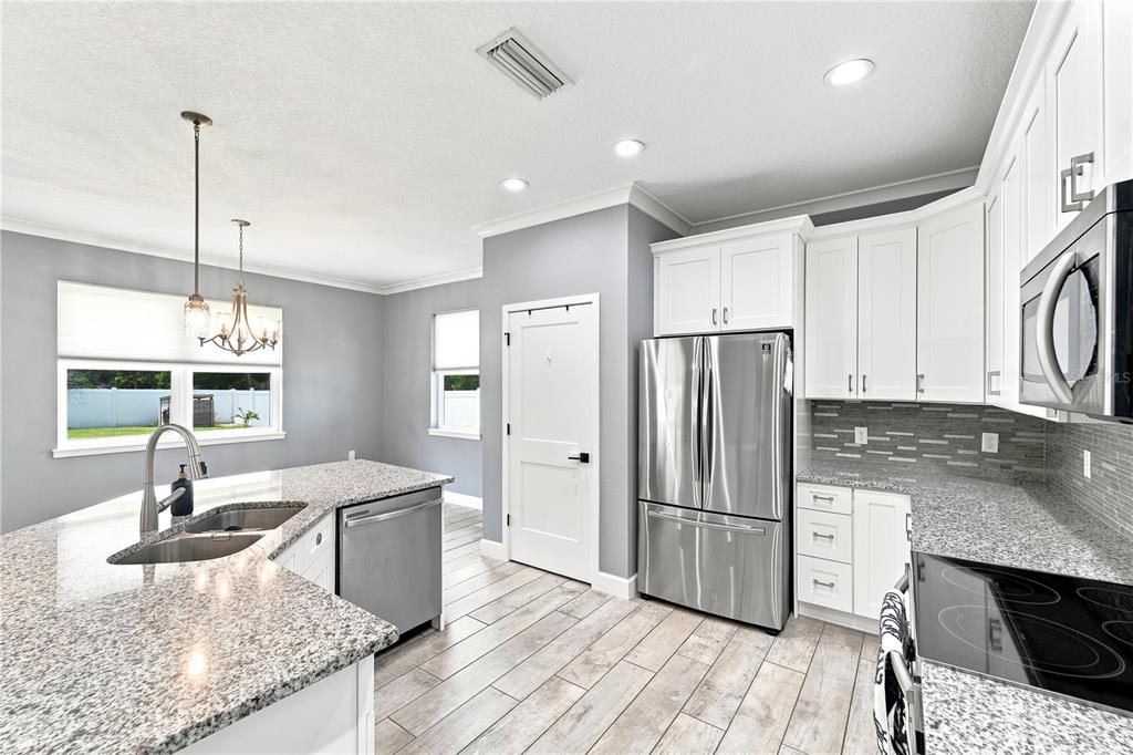 A modern kitchen features white cabinets, granite countertops, stainless steel appliances, and wood-look tile flooring — 125 LONGWOOD DRIVE, OSTEEN, FL
