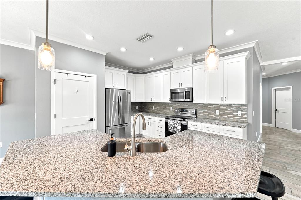 A kitchen features a granite-topped island, white cabinetry, stainless steel appliances, and gray walls — 125 LONGWOOD DRIVE, OSTEEN, FL
