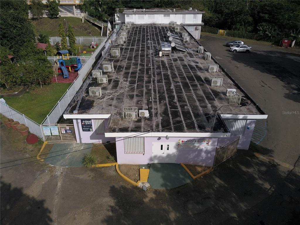 An aerial view shows a light purple building with a flat roof and playground area — PR 181 Km 4.8 BO. LAS CUEVAS, TRUJILLO ALTO, PR