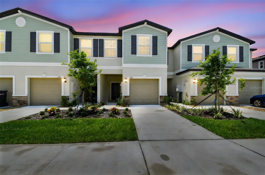 A row of three attached townhouses with light green siding, tan garage doors, and concrete driveways — 2665 BUTTERCUP LUCINE LANE, RUSKIN, FL