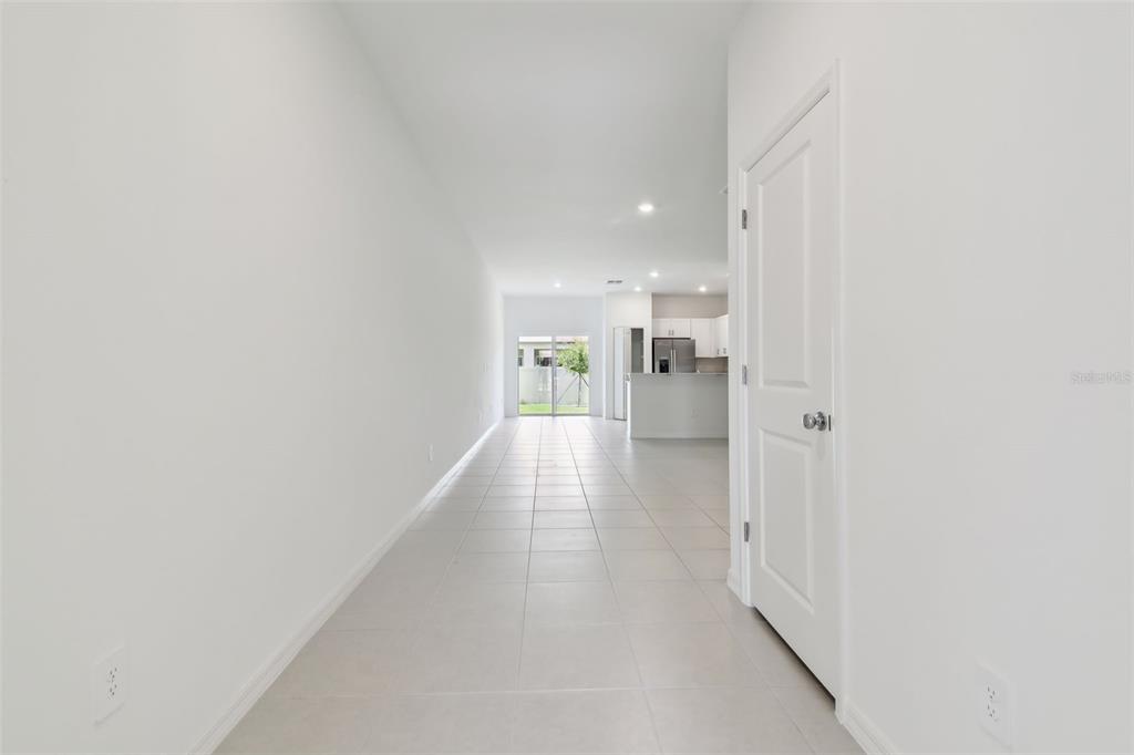 A long, tiled hallway leads toward an open-concept kitchen and a glass sliding door — 2665 BUTTERCUP LUCINE LANE, RUSKIN, FL