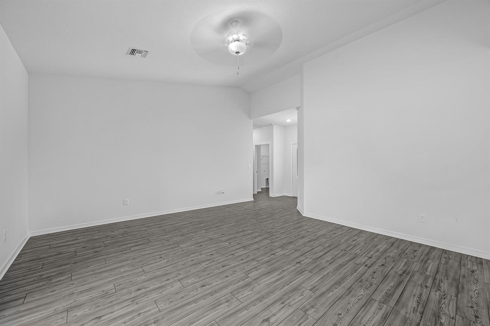 An empty room features white walls, a ceiling fan, and gray wood-look flooring — 8446 104th Court, Vero Beach FL 32967, VERO BEACH, FL