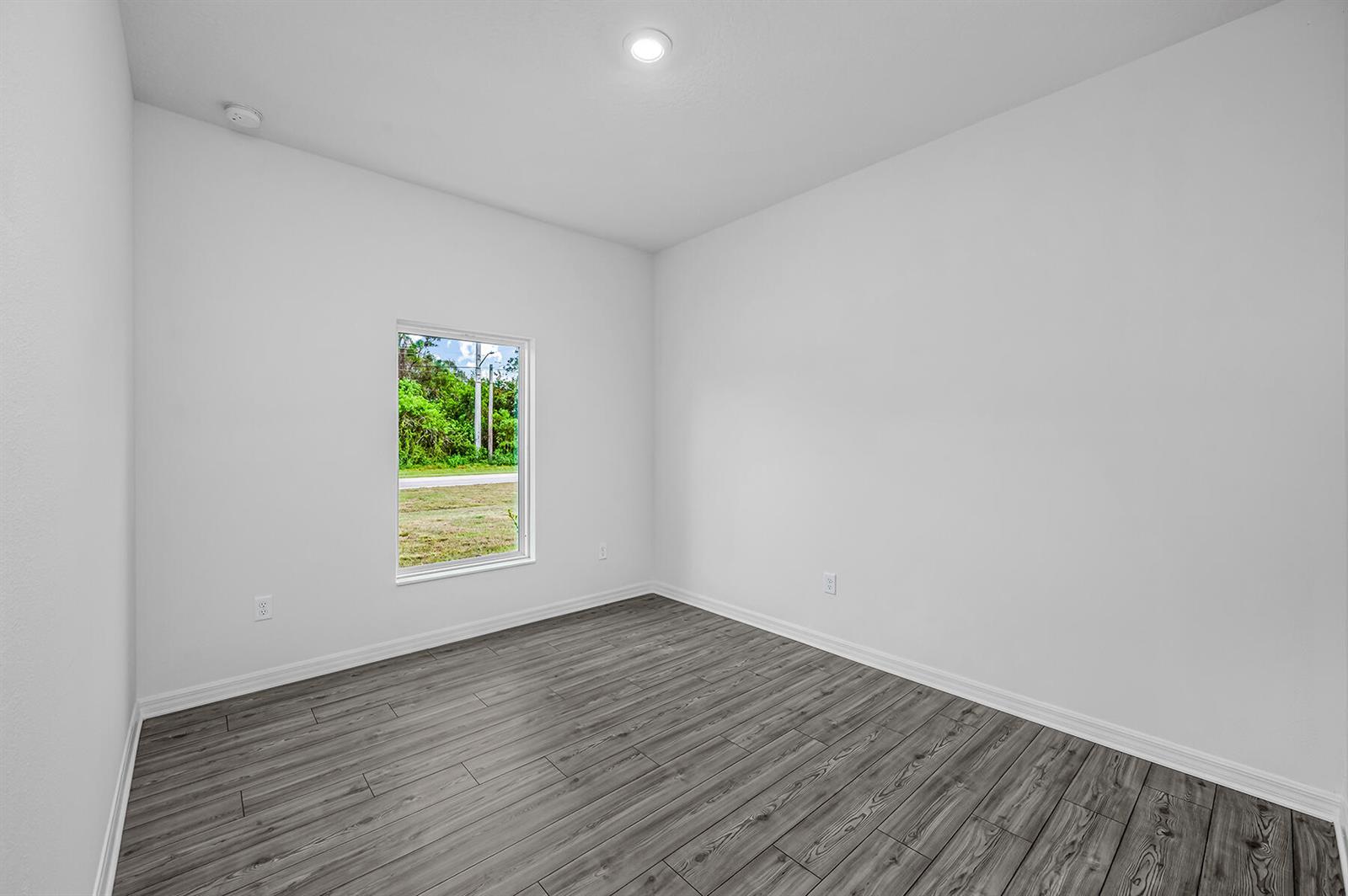 An empty room with white walls, gray wood-look flooring, and a single window — 8446 104th Court, Vero Beach FL 32967, VERO BEACH, FL