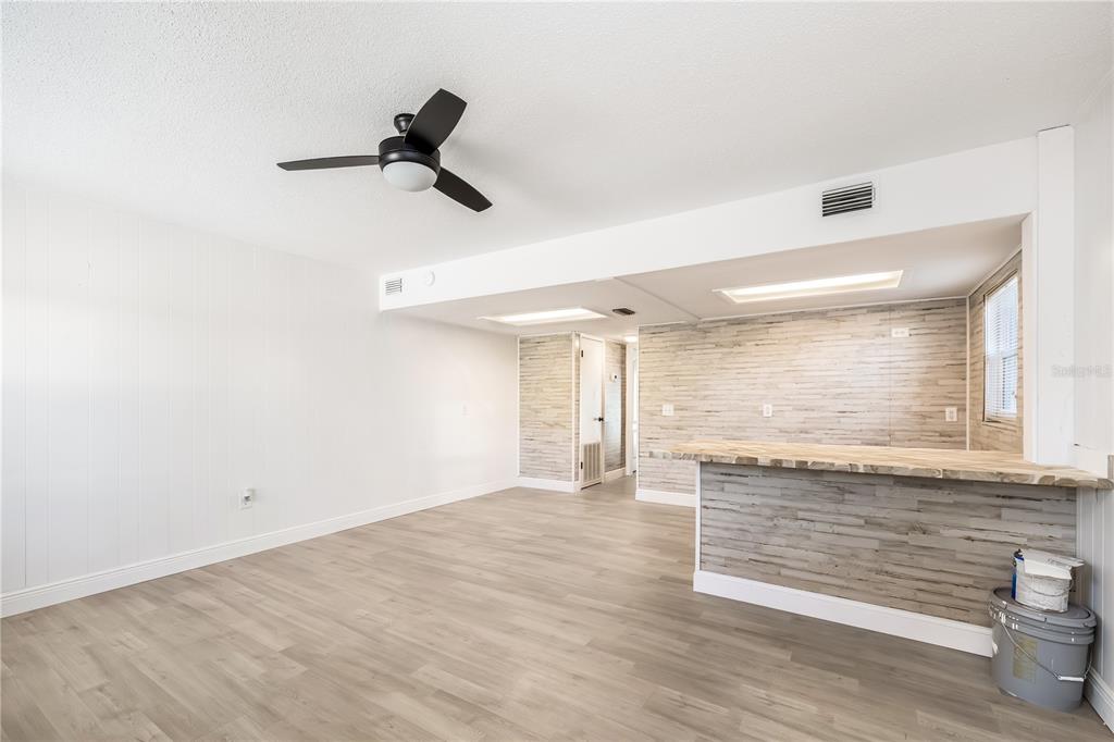 A living room with light wood-look flooring, a ceiling fan, and a wood-paneled breakfast bar — 212 S DAYTONA AVENUE UNIT 2, FLAGLER BEACH, FL