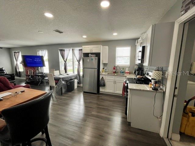 An open-concept kitchen and dining area features wood-look flooring, white cabinetry, and a stainless refrigerator — 118 W STUART AVENUE, LAKE WALES, FL