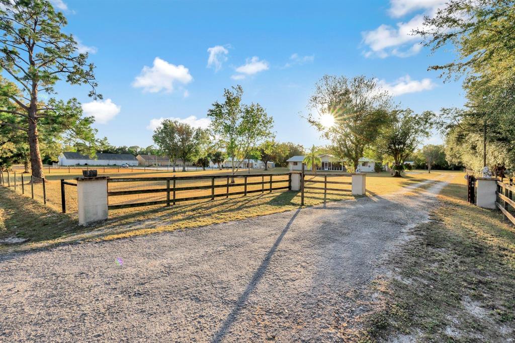 A gravel driveway leads to a gated entrance with wooden fencing and mature trees — 16321 SLATER ROAD, NORTH FORT MYERS, FL