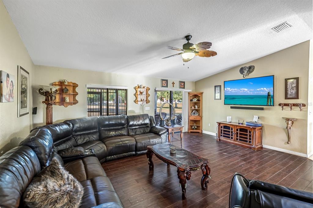 A living room features a large leather sectional, dark wood flooring, and a wall-mounted television — 16321 SLATER ROAD, NORTH FORT MYERS, FL