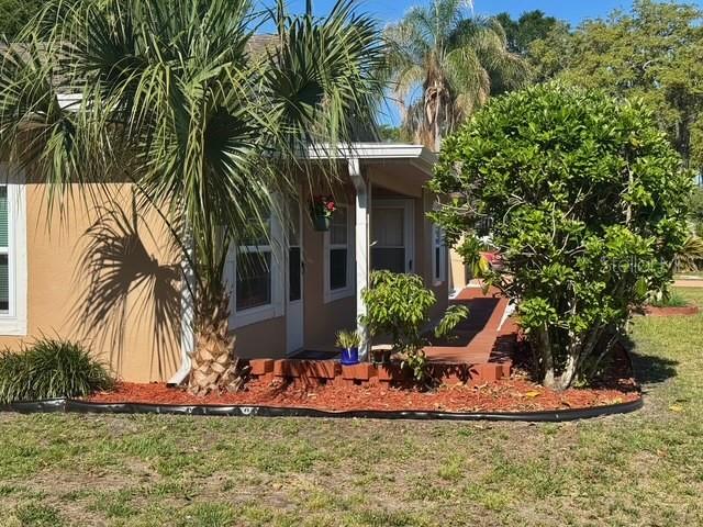 A tan house exterior features a covered porch, a palm tree, and a large green bush — 910 W FRENCH AVENUE, ORANGE CITY, FL