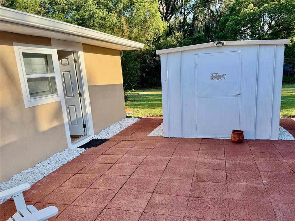A tan exterior wall with a white door and window sits beside a white shed — 910 W FRENCH AVENUE, ORANGE CITY, FL