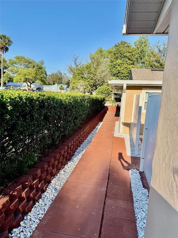 A red concrete walkway runs alongside a retaining wall and a hedge next to a house — 910 W FRENCH AVENUE, ORANGE CITY, FL
