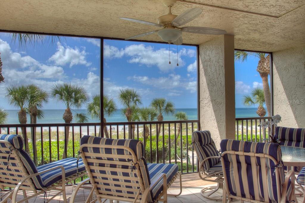 A screened-in balcony features striped patio furniture, a ceiling fan, and a view of palm trees — 1925 GULF OF MEXICO DRIVE UNIT G8-208, LONGBOAT KEY, FL