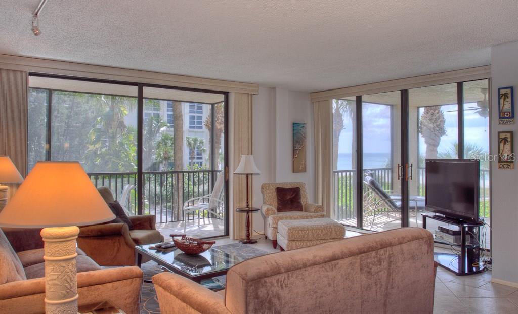 A living room with beige furniture, a glass coffee table, and sliding doors overlooking the ocean — 1925 GULF OF MEXICO DRIVE UNIT G8-208, LONGBOAT KEY, FL