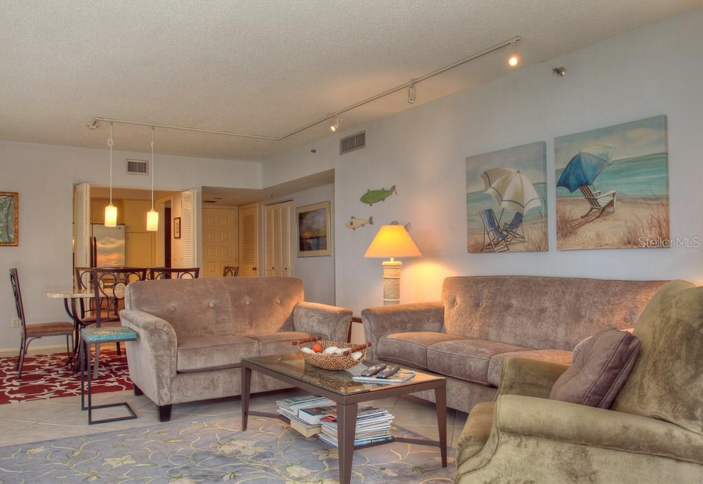 A living room with two beige sofas, a glass coffee table, and beach-themed wall art — 1925 GULF OF MEXICO DRIVE UNIT G8-208, LONGBOAT KEY, FL