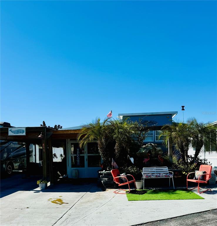 A mobile home exterior features a covered carport, palm trees, and a small patio area — 411 ST GEORGE DRIVE, DAVENPORT, FL