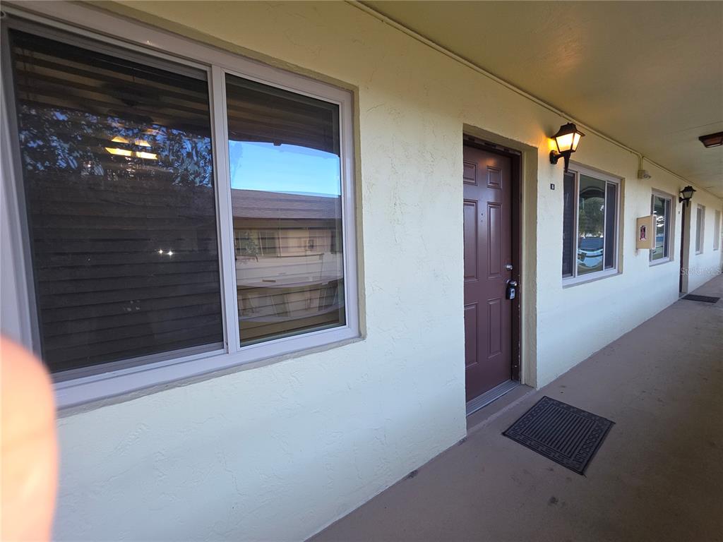 An exterior view of a building walkway featuring a brown door and a large window — 400 OAKRIDGE BOULEVARD UNIT 60, DAYTONA BEACH, FL