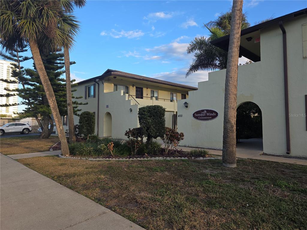 A two-story tan condominium building with palm trees and a sidewalk in the foreground — 400 OAKRIDGE BOULEVARD UNIT 60, DAYTONA BEACH, FL