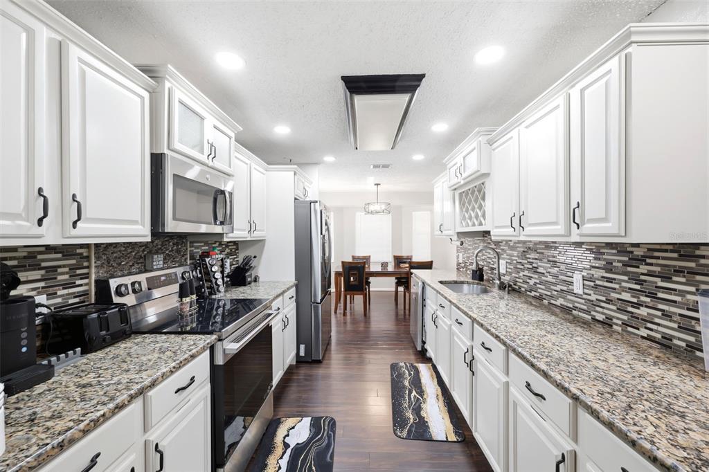 A galley kitchen features white cabinets, granite countertops, a tiled backsplash, and stainless steel appliances — 5552 W IRVING COURT, HOMOSASSA, FL