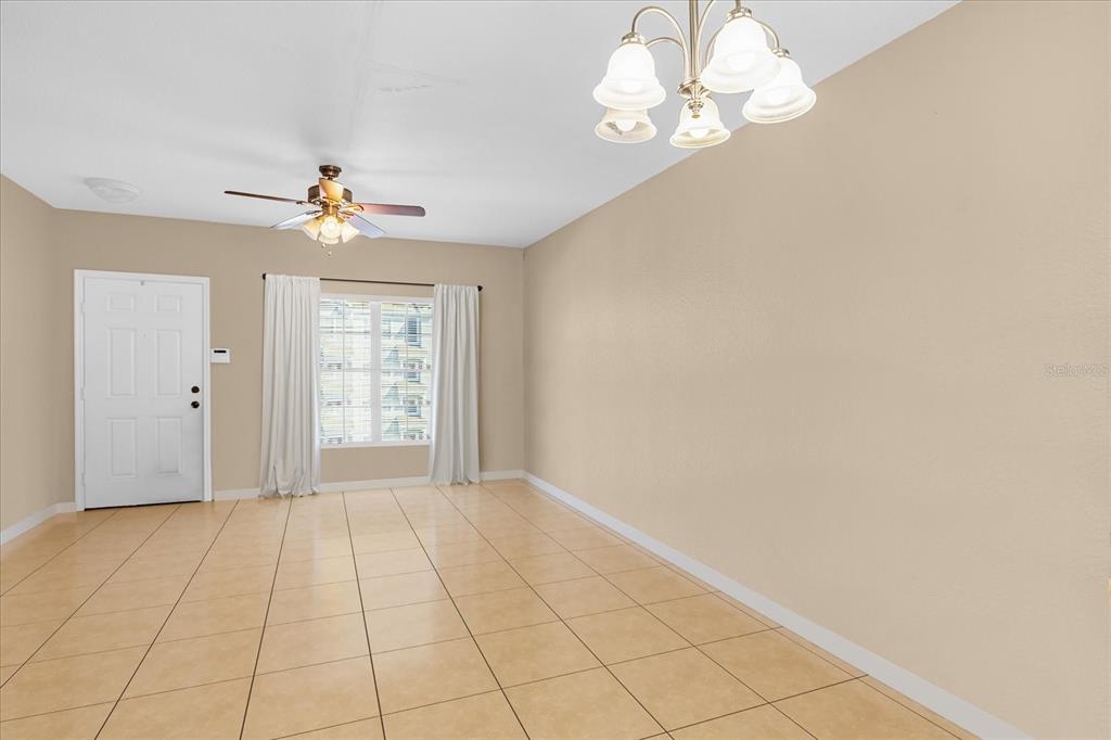 An empty room features beige tile flooring, a ceiling fan, and a chandelier — 727 SHROPSHIRE LOOP, SANFORD, FL